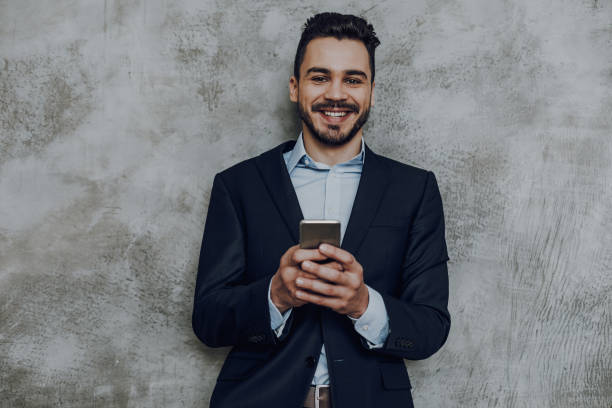istock Happy elegant man with smartphone against grey wall 1149340706