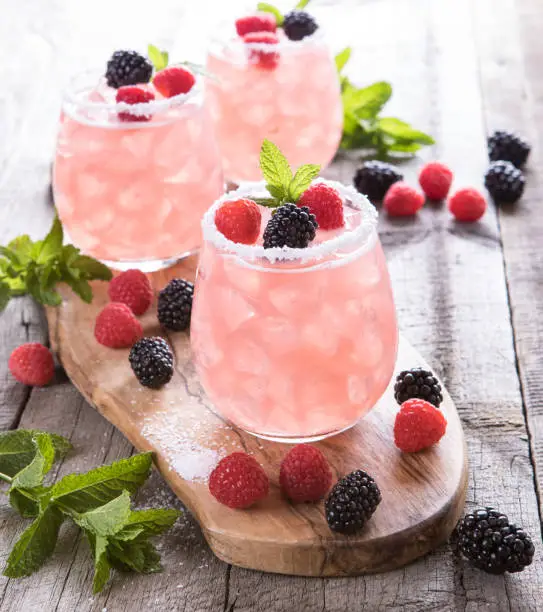 Three pink refreshing summer fruit drinks with fresh fruit salt rim