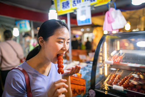 young woman eating sugar coated tomato in Taipei night market