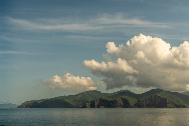 Rinca Island, Indonesia - February 24, 2019: Early morning. Southside coast in Savu Sea under cloudscape with white and darker patches.Green hills and cliffs.