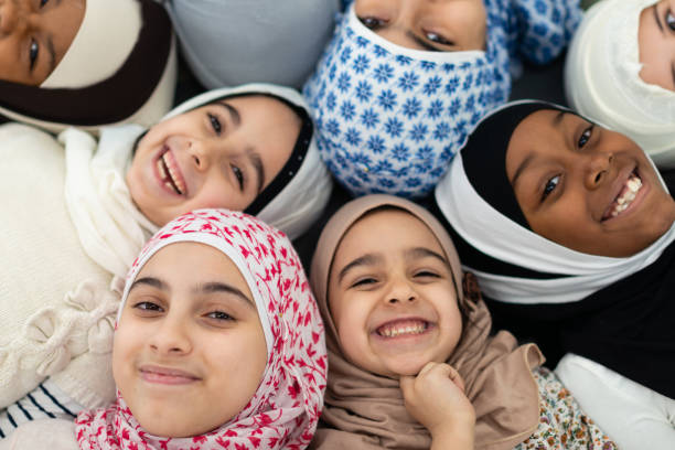 Smiling Muslim overhead portrait An adorable group of muslim kids wearing hijabs smile in this overhead portrait taken in their classroom. They are all laying close to each other exuding joy. pics of a cute muslim outfits stock pictures, royalty-free photos & images