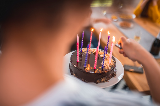 Close-up of woman igniting candles on cake. Female is holding birthday cake. She is at home.