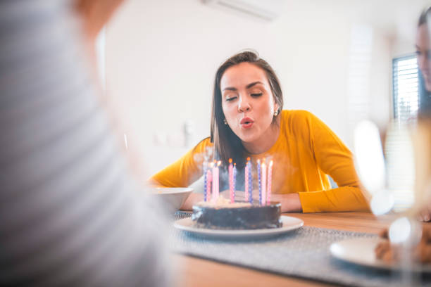 Beautiful woman blowing candles on birthday cake Beautiful young woman blowing candles on cake at dining table. Females are celebrating birthday party of friend. They are at home. woman birthday cake stock pictures, royalty-free photos & images