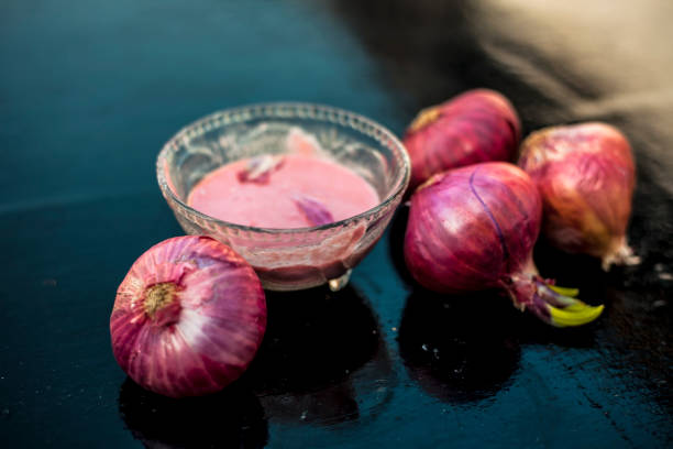 Close up of glass bowl full of extracted onion pulp in it and raw onions or pyaaj or Allium cepa. stock photo