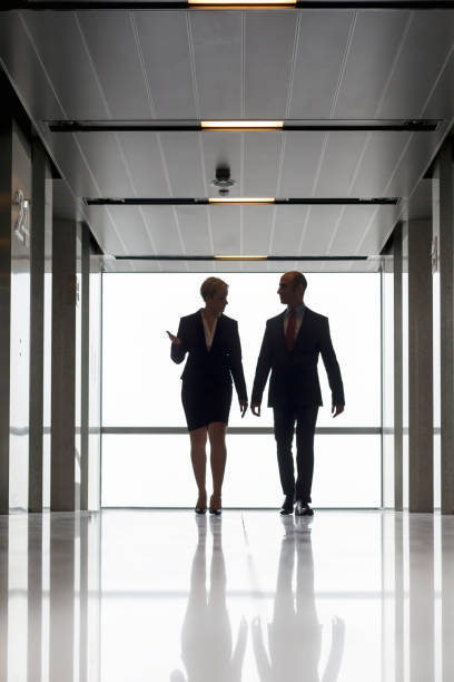 istock Full length of mature colleagues talking while walking against window in office corridor 1149377520
