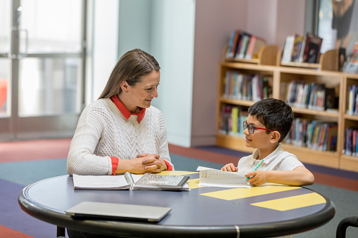 High quality stock photo of one on one tutoring in a library and classroom with authentic instructor and 8 year old child student.