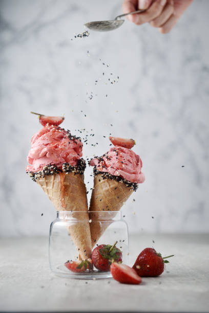 Strawberry ice cream cone in glass decorated with black sesame sprinkles and fresh strawberry on top on marble background.