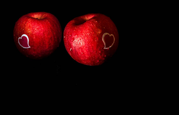 pegatina de forma de corazón y gota de agua en la superficie brillante de manzana roja sobre fondo negro - drop red delicious apple apple fruit fotografías e imágenes de stock