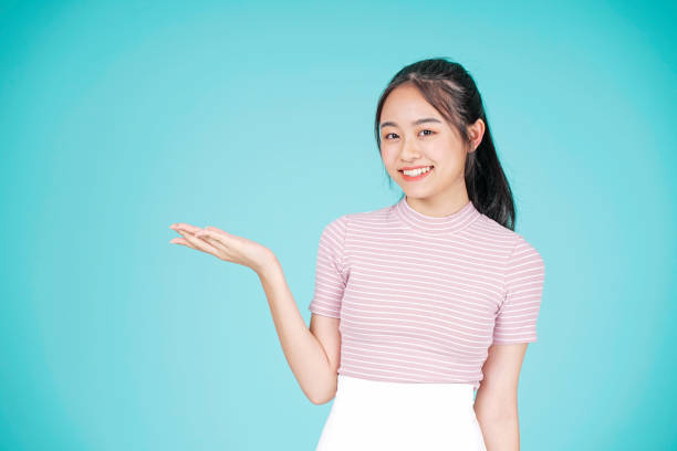 Asian young teenage attractive beautiful girl with hand showing information on cyan color background Asian young teenage attractive beautiful girl with hand showing information on cyan color background vietnamese girls for sale stock pictures, royalty-free photos & images