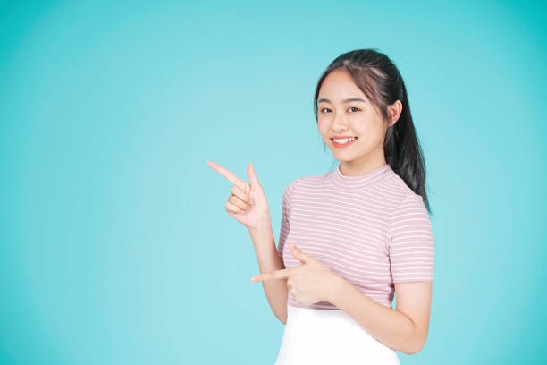 Asian young teenage attractive beautiful girl with hand showing information on cyan color background Asian young teenage attractive beautiful girl with hand showing information on cyan color background vietnamese girls for sale stock pictures, royalty-free photos & images