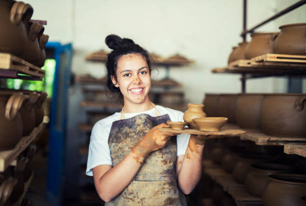 Portrait of teenager holding clay vessels at workshop. Teenager girl working in family factory for pottery, she holding clay vessels, workshop pottery making stock pictures, royalty-free photos & images