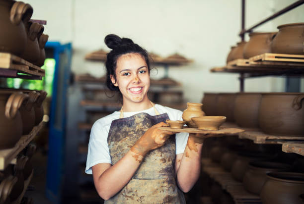 Portrait of teenager holding clay vessels at workshop. Teenager girl working in family factory for pottery, she holding clay vessels, workshop career girl stock pictures, royalty-free photos & images