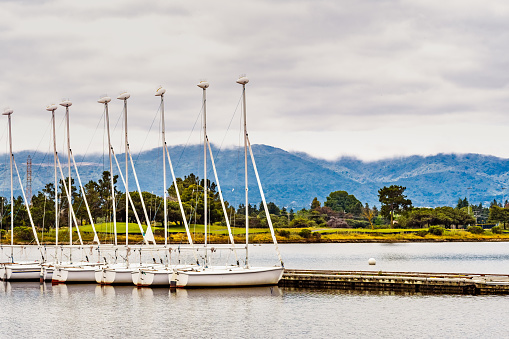 Rental sailing boats lined up on a pier in South San Francisco bay area, Shoreline Lake and Park; Santa Cruz mountains visible in the background; Mountain View, California