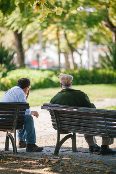 istock Rear View Of Men Sitting On Bench In Park 1149438061