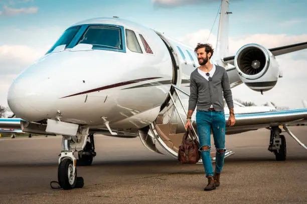 Rich, fashionable man walking away from a private jet parked on an airport runway.