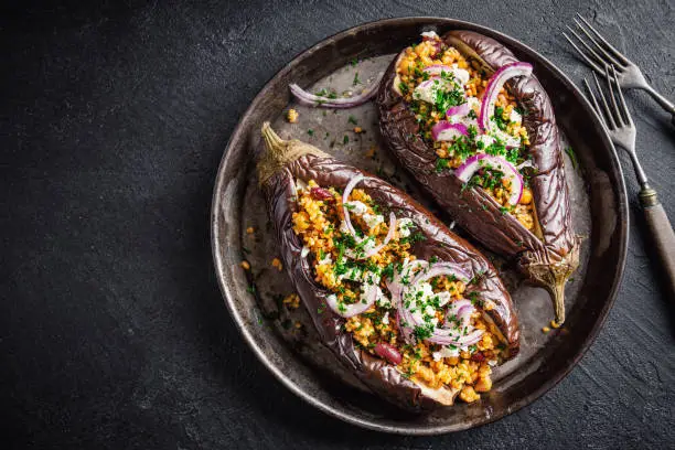 Healthy tasty baked aubergine with bulgur, chickpea, spices, onion and feta served on grey background. Top View.