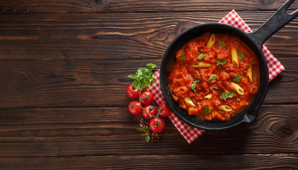 istock Pasta penne with tomato sauce and basil on iron cast pan. Wooden table, top view with copy space 1149451836