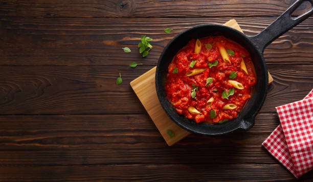 istock Pasta penne with tomato sauce and basil on iron cast pan. Wooden table, top view with copy space 1149451919