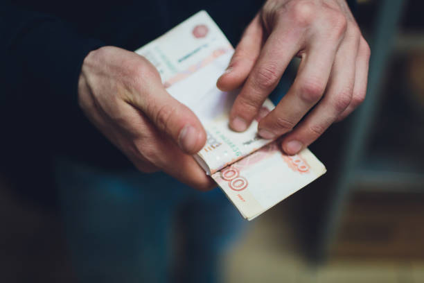 istock man giving money, Russian Ruble banknotes, over his desk in a dark office - bribery and corruption concept.russian rubles banknotes. Financial theme.stack of banknotes in a man's hand. 1149457607
