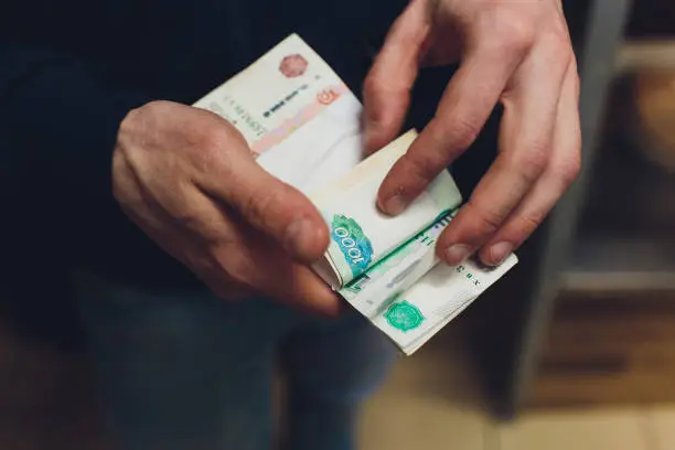 man giving money, Russian Ruble banknotes, over his desk in a dark office - bribery and corruption concept.russian rubles banknotes. Financial theme.stack of banknotes in a man's hand