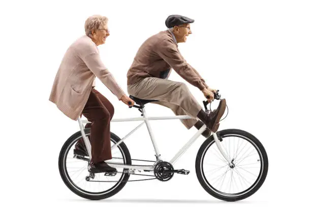 Full length shot of a senior man and woman riding a tandem bicycle with legs up isolated on white background