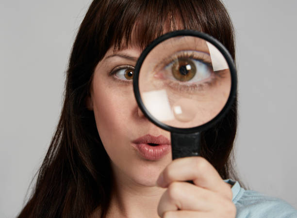 istock Brunette looks through magnifying glass at camera, enlarging her eye 1149459513
