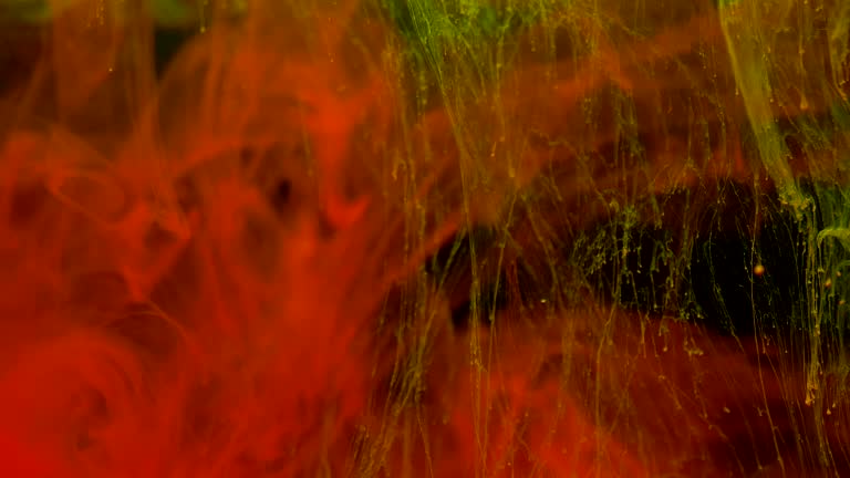 Red and yellow color paint inks diffuse in water in slow motion on black background with inky cloud swirling and abstract smoke explosion.