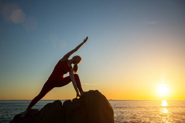 Yoga silhouette young woman doing fitness exercises in the posture of the asana of the elongated triangle on the beach at amazing sunset. Yoga silhouette young woman doing fitness exercises in the posture of the asana of the elongated triangle on the beach at amazing sunset. yoga stock pictures, royalty-free photos & images