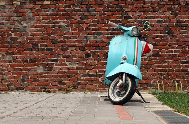 an iconic vintage blue vespa scooter parked. old brick wall on background - vespa scooter imagens e fotografias de stock