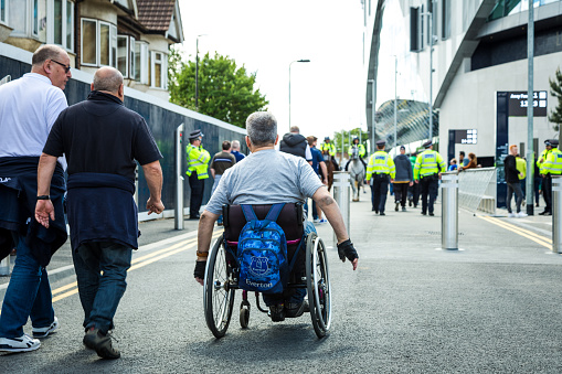 London, UK - 12 May, 2019: color image depicting disabled football supporters in wheelchairs outside the brand new modern architecture of the Tottenham Hotspur stadium in north London, UK. It is the day of an English Premier League match (Tottenham v Everton) and the fans are eager to explore the surroundings of the new stadium. Room for copy space.
