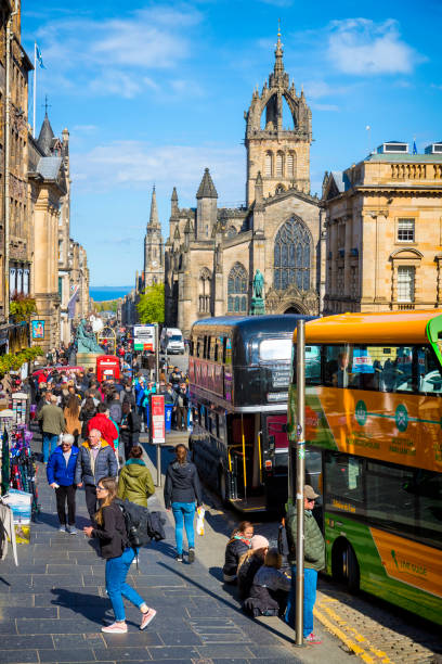 Double Decker Tour Buses and crowds of people along the historic Royal Mile in the Edinburgh's Old Town, on the horizon the North Sea