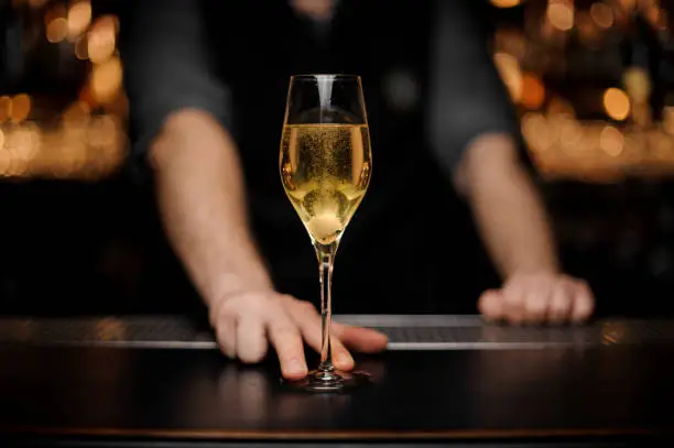 Close-up of glass with sparkling wine on the bar counter in the male bartender's hands