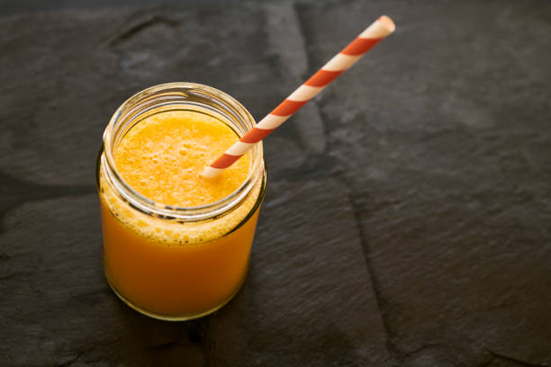Mason Jar filled with fresh Orange Juice, with straw on a slate background.