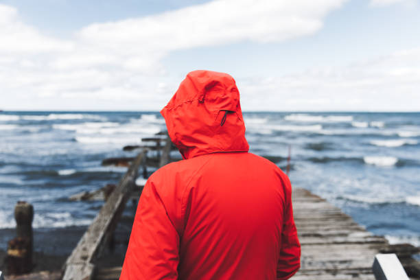 Young man in red jacket enjoying the view of stormy ocean staying near the pier in Punta Arenas, Patagonia, Chile