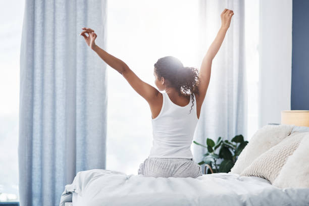 It's a good morning to me Rearview shot of an unrecognizable young woman stretching while sitting on her bed in the morning waking up photos stock pictures, royalty-free photos & images