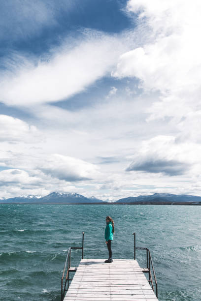 woman stays on the pier looking at the ocean and mountains in puerto natales - puerto de sol imagens e fotografias de stock