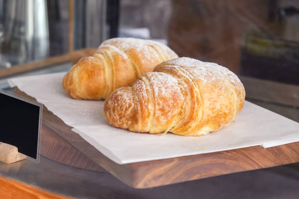 Close up two pieces of fresh croissants above wooden tray in cafeteria display