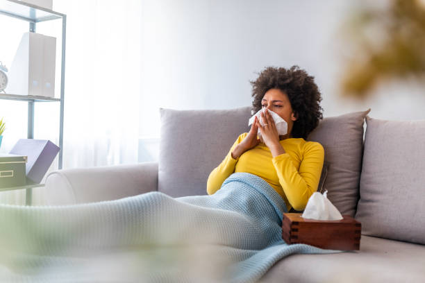 Picture showing sick woman sneezing at home The sick woman, holding a handkerchief, sneezing and feeling freezing, lying on the bed, at home. Health problem. Sick African American woman lying on the sofa facial tissue stock pictures, royalty-free photos & images