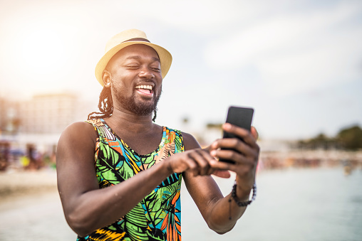 Cheerful African man using a phone while on a beach.