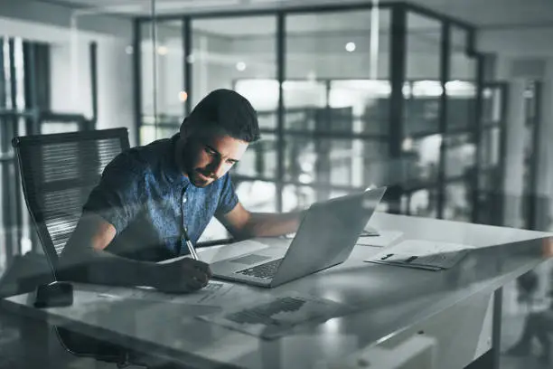 Cropped shot of a handsome young businessman working late at night at his desk in the office