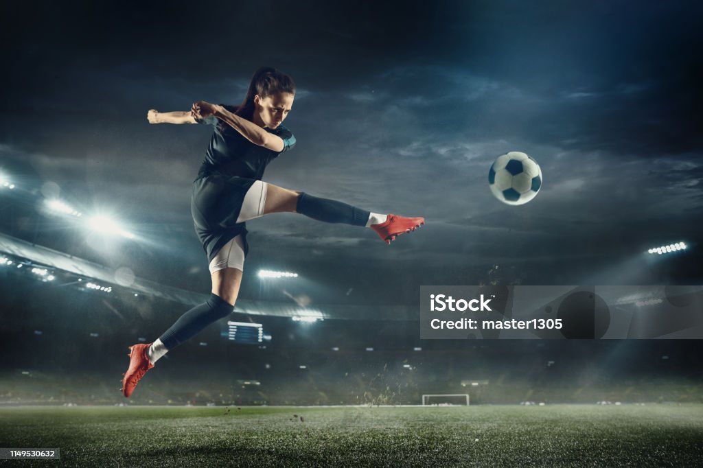 Female soccer player kicking ball at the stadium Young female soccer or football player with long hair in sportwear and boots kicking ball for the goal in jump at the stadium. Concept of healthy lifestyle, professional sport, hobby, motion, movement. Soccer Stock Photo