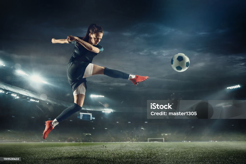 Jogador de futebol fêmea que retrocede a esfera no estádio - Foto de stock de Futebol royalty-free