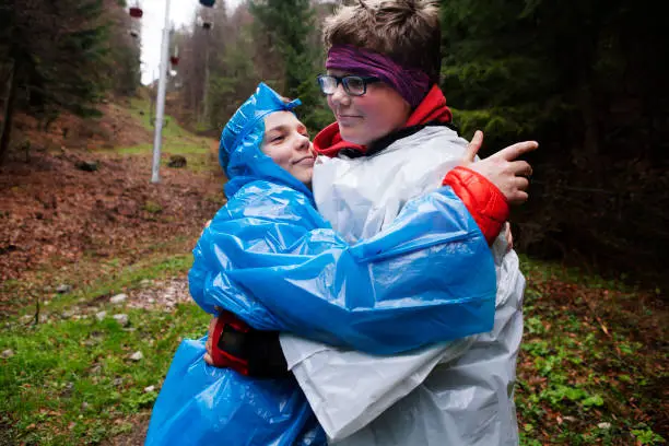 Tatranska Lomnica, Slovakia - April 30, 2019: teenager brothers wearing rain ponchos standing in rain and making poses, faces and fun.