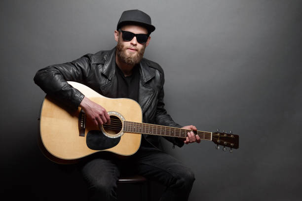 istock Guitar player singing in music studio. Hipster guitar player with beard and black clothes playing the acoustic guitar 1149534147