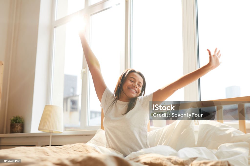Mixed Race Woman Enjoying Morning Portrait of beautiful Mixed-Race woman stretching sitting in bed lit by sunlight, copy space Sleeping Stock Photo