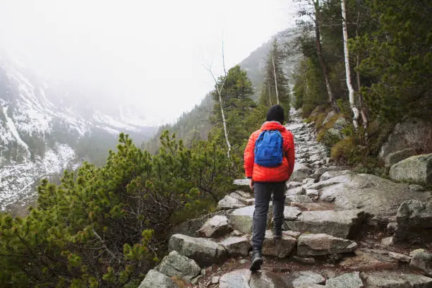 Stary Smokoves, Slovakia - April 28, 2019: teenager boy is hiking in mountains on a cold day wearing his red warm jacket