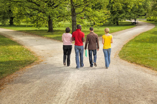 istock Group of four multi-ethnic students walking on forked road in public park 1149539375