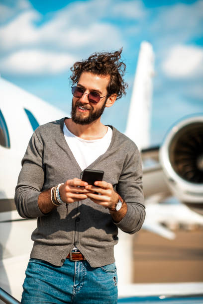 istock Young rich man using a smart phone while disembarking outside of the private airplane parked on a runway 1149539450