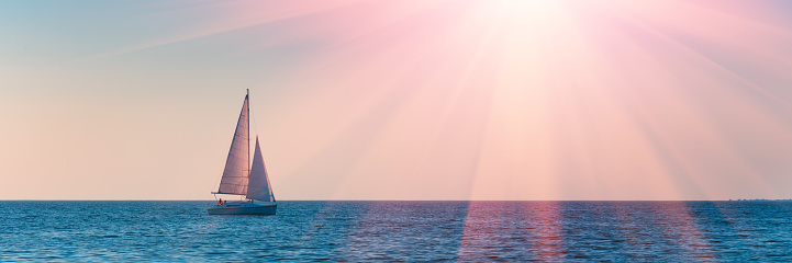 Banner 3:1. Sailboat in the sea in the evening sunlight over sky background. Luxury summer adventure or active vacation concept. Copy space.