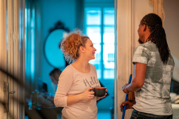 Young African-American man with broomstick talking to female flatmate Young African-American man holding broomstick and beer bottle, talking to his female Caucasian flatmate flatmate stock pictures, royalty-free photos & images